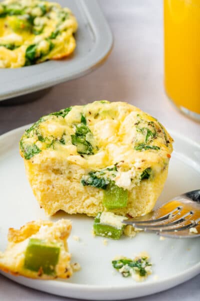 A spinach feta egg muffin on a plate with a bite taken out.