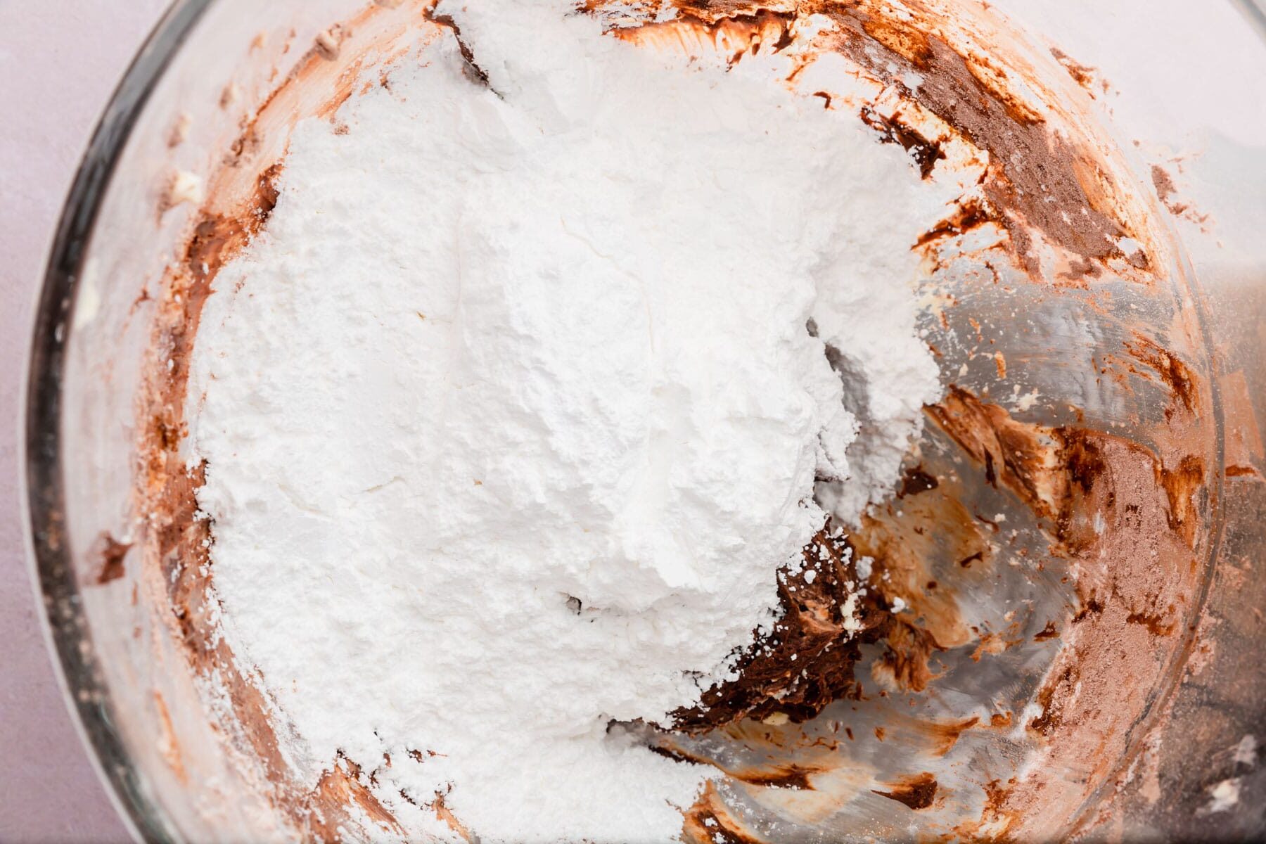 Powdered sugar being added to a bowl of chocolate cream cheese frosting.