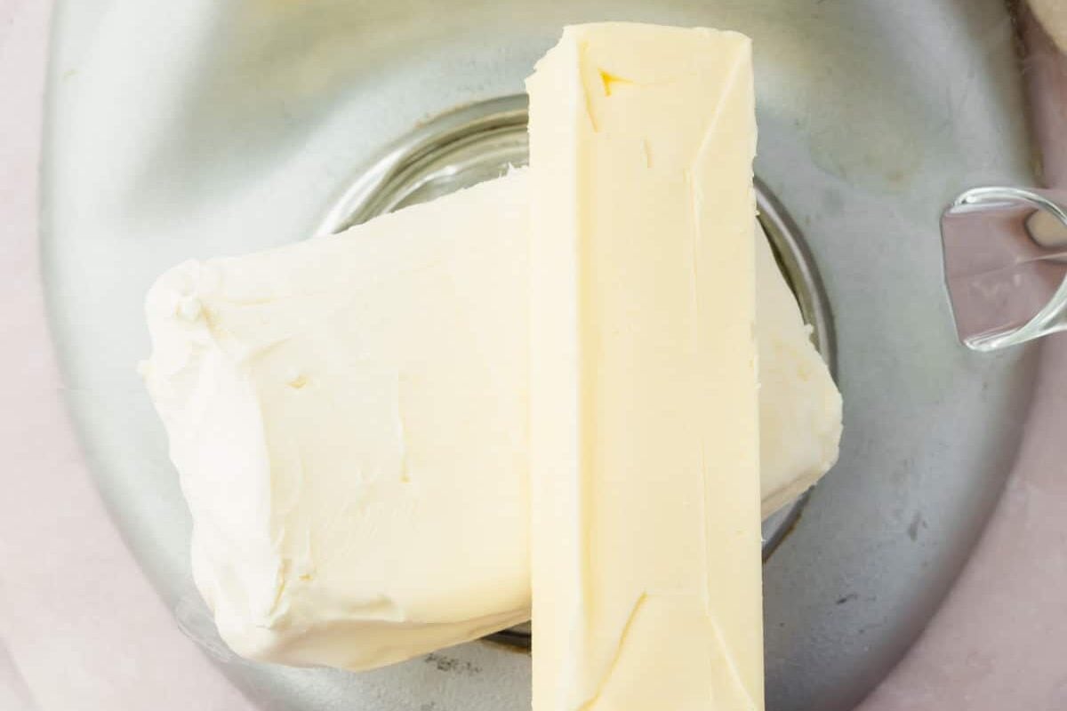 A stick of butter and a block of cream cheese in a mixing bowl.
