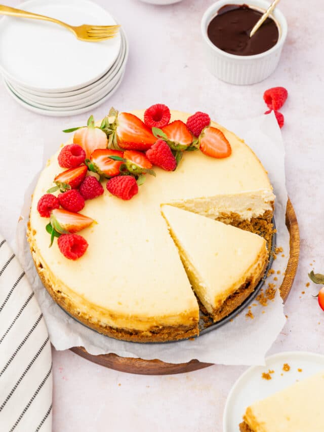 A gluten-free cheesecake topped with red berries with a slice already cut out of it.