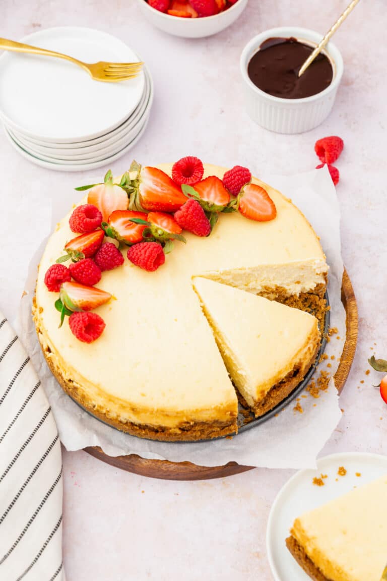 A gluten-free cheesecake topped with red berries with a slice already cut out of it.