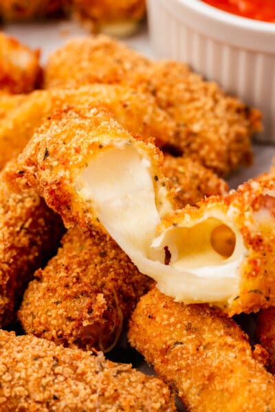 A close-up of a gluten-free mozzarella stick broken open to show the oozing cheese.