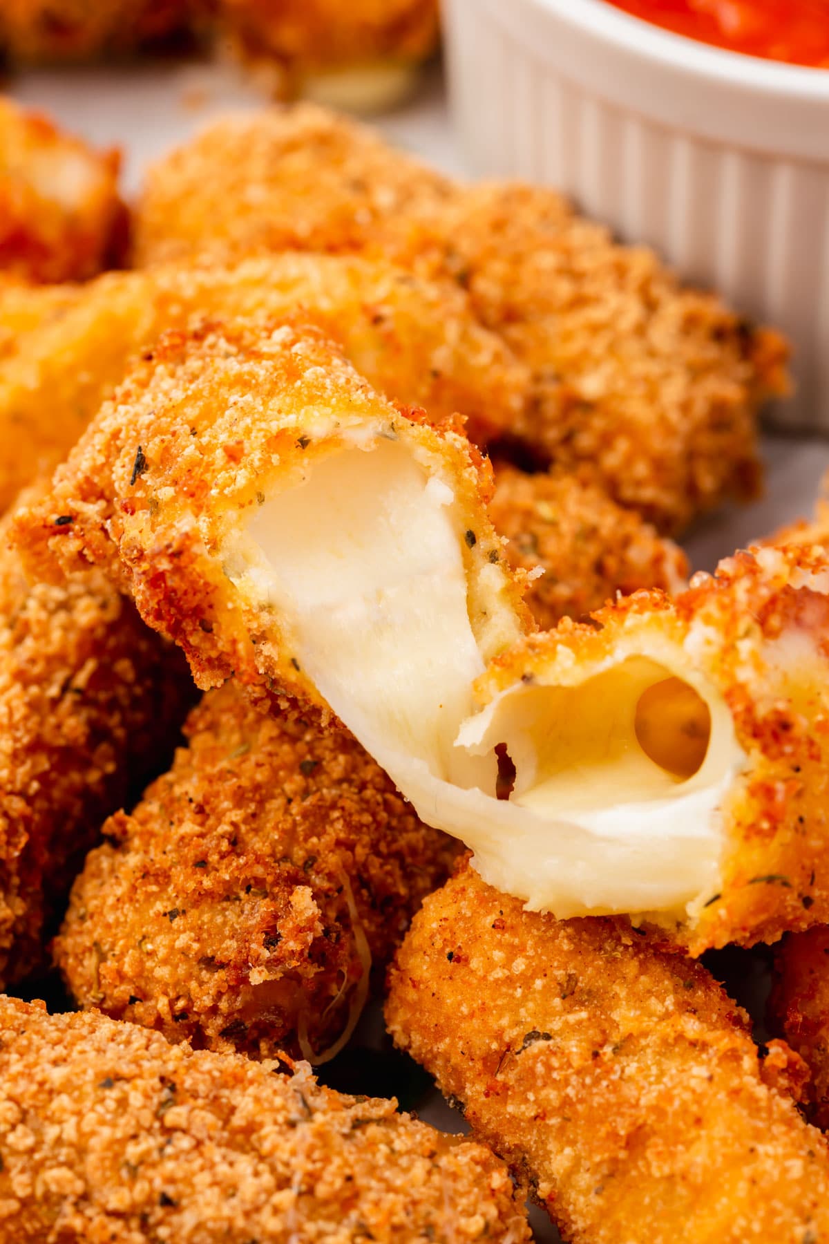 A close-up of a gluten-free mozzarella stick broken open to show the oozing cheese.