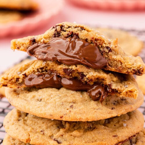 A pile of gluten-free Nutella stuffed peanut butter cookies with the top cookie split in half and stacked atop one another to show the gooey Nutella filling.