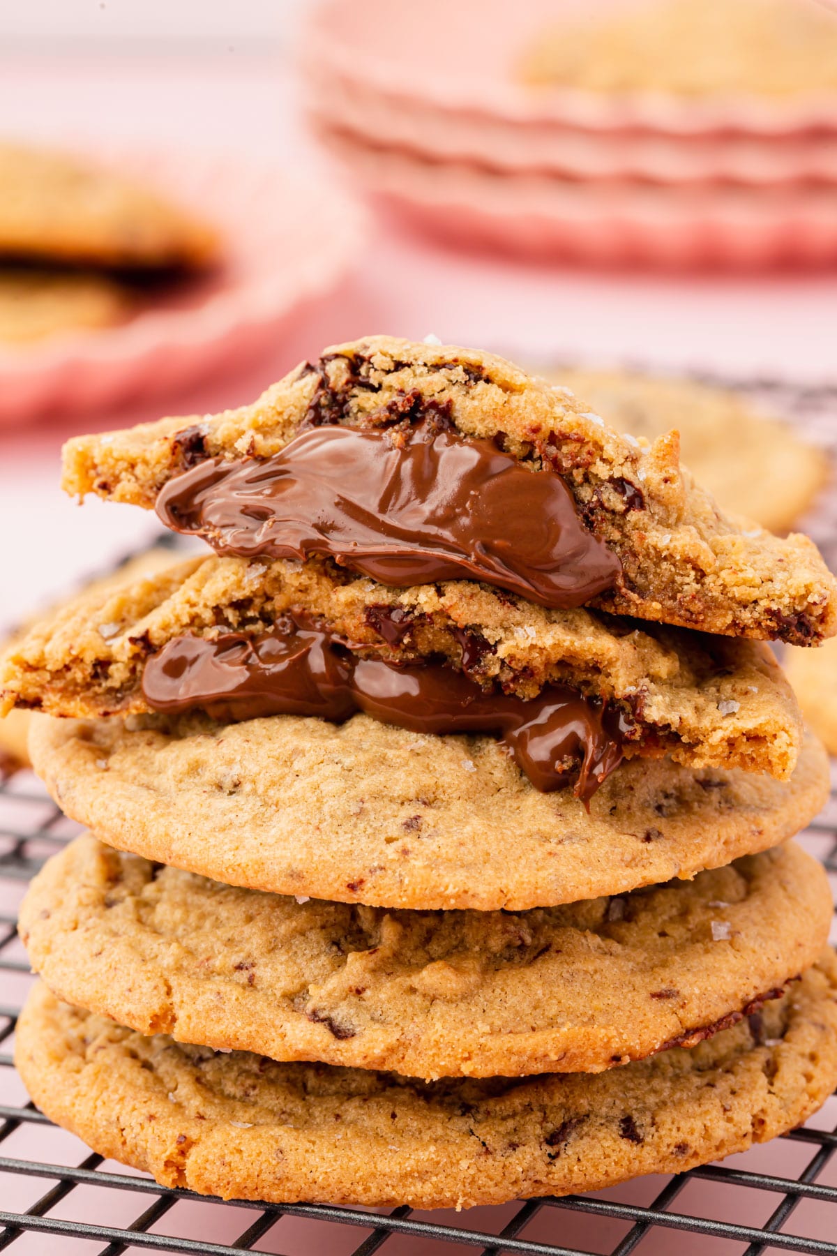 A pile of gluten-free Nutella stuffed peanut butter cookies with the top cookie split in half and stacked atop one another to show the gooey Nutella filling.