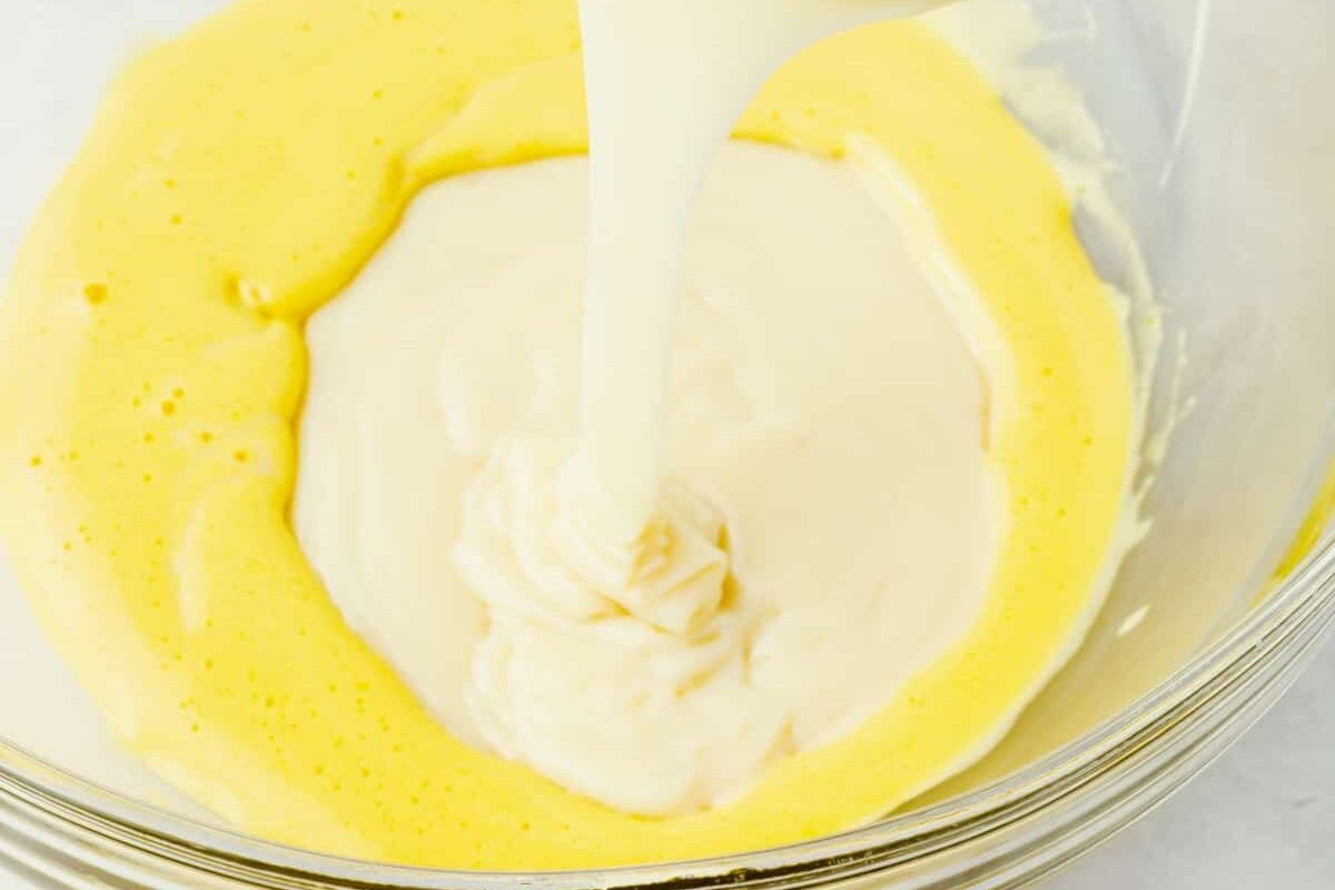 Sweetened condensed milk being poured into a mixing bowl of whisked egg yolks to make a key lime pie custard.