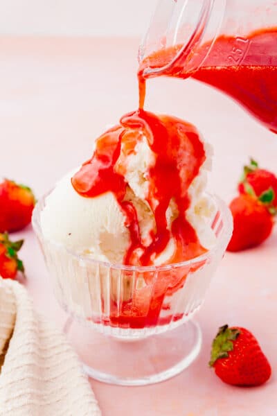 A bowl of vanilla ice cream being topped with strawberry coulis.