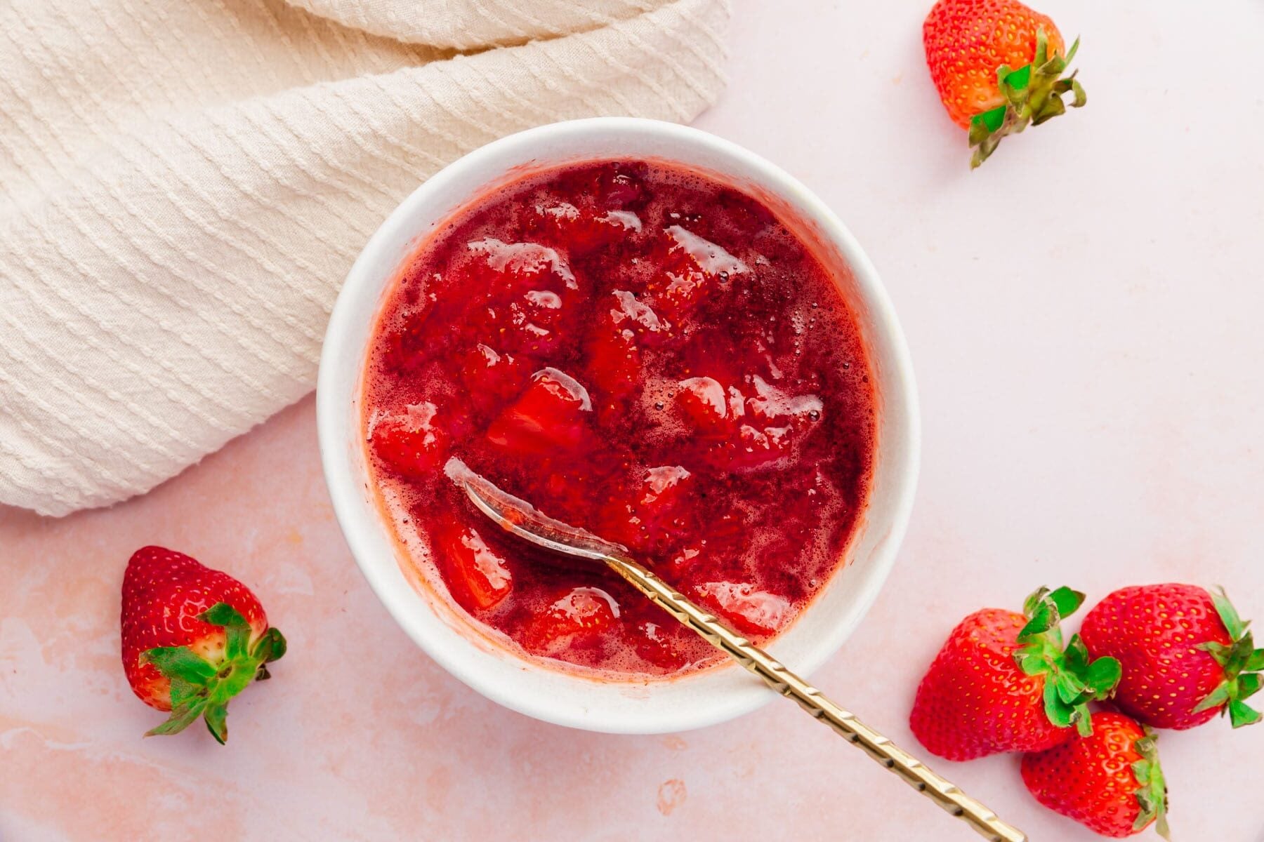 A bowl of chunky strawberry coulis surrounded by fresh strawberries.