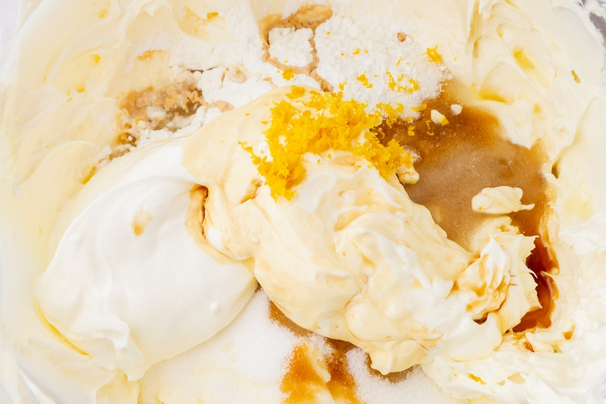 A close-up of ingredients in a mixing bowl, including cream cheese, sugar, vanilla extract, sour cream, and lemon zest—perfect for making a delicious gluten free cheesecake.