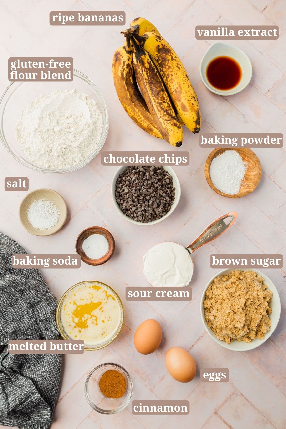 Ingredients for making gluten-free banana bread: ripe bananas, gluten-free flour blend, vanilla extract, salt, chocolate chips, baking soda, baking powder, sour cream, melted butter, brown sugar, eggs, and cinnamon.
