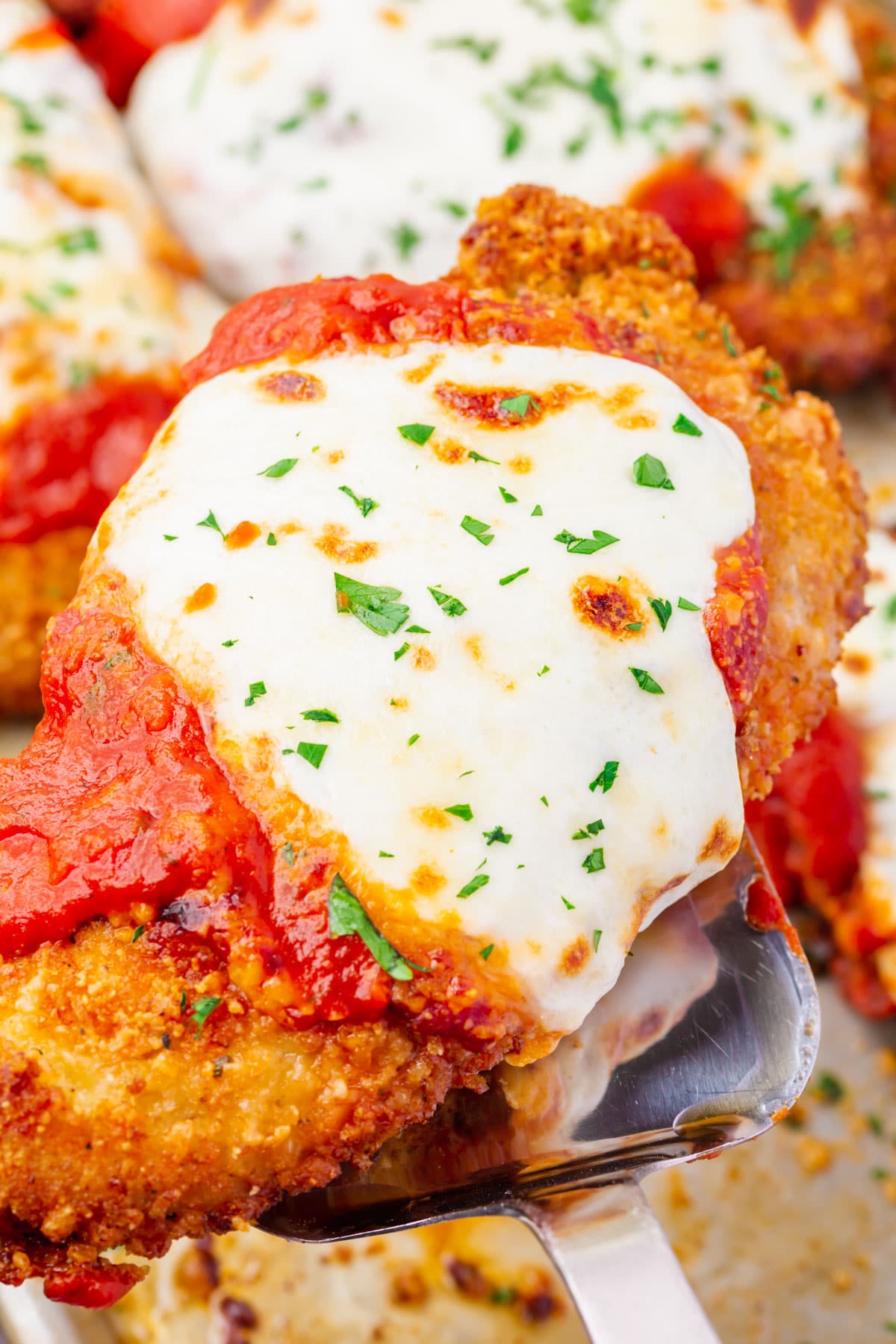 A piece of Gluten-Free Chicken Parmesan being lifted off a baking tray with a silver spatula.