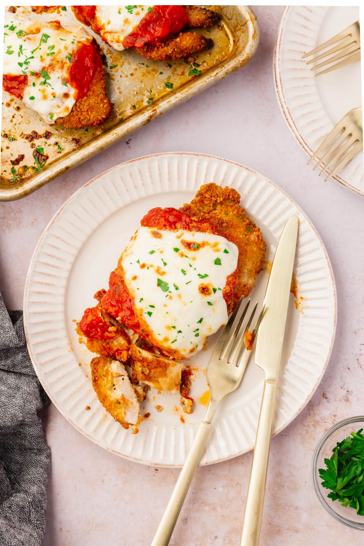 A piece of Gluten-Free Chicken Parmesan on a plate with a fork and knife.