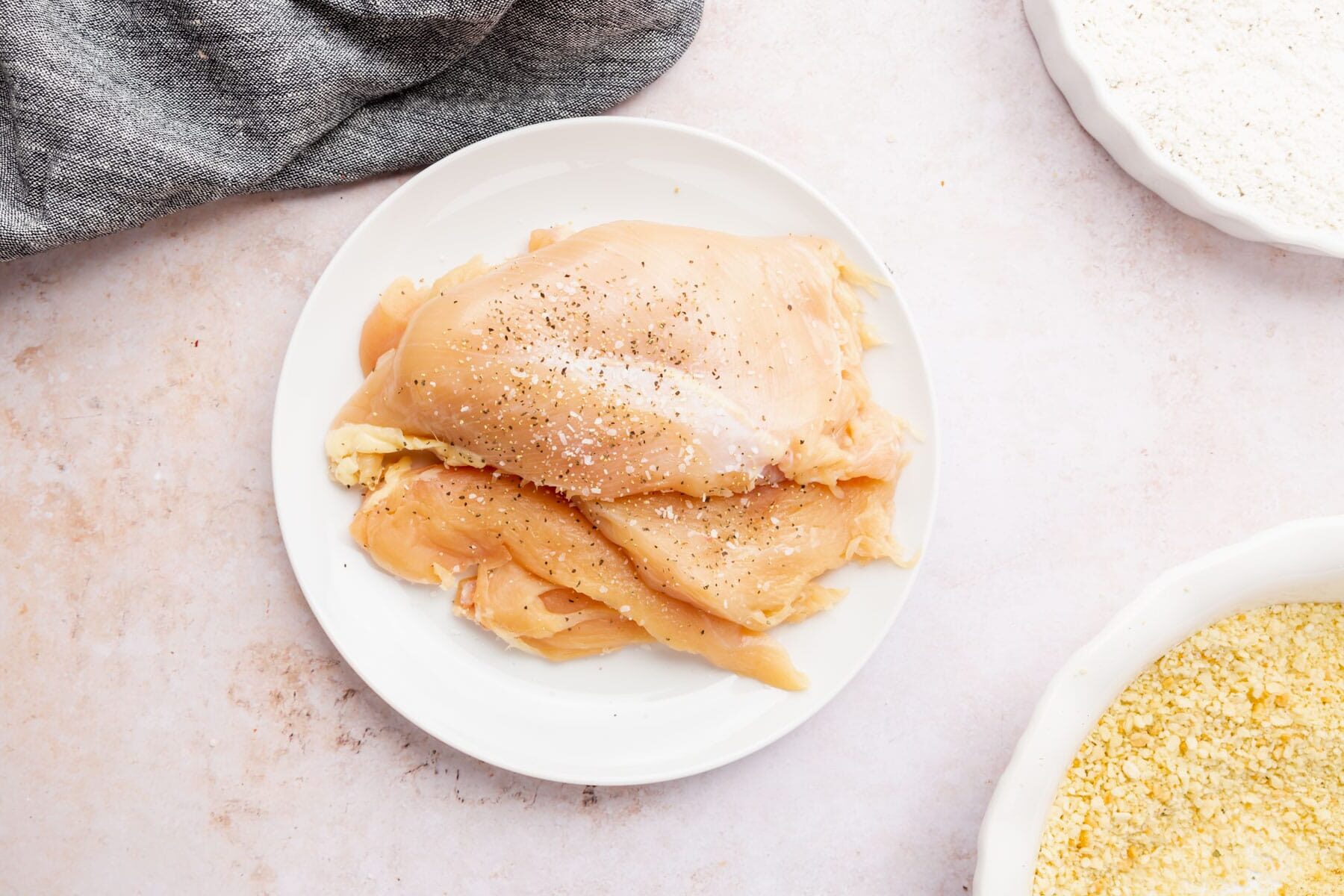 A plate of boneless skinless chicken breasts seasoned with salt and pepper.