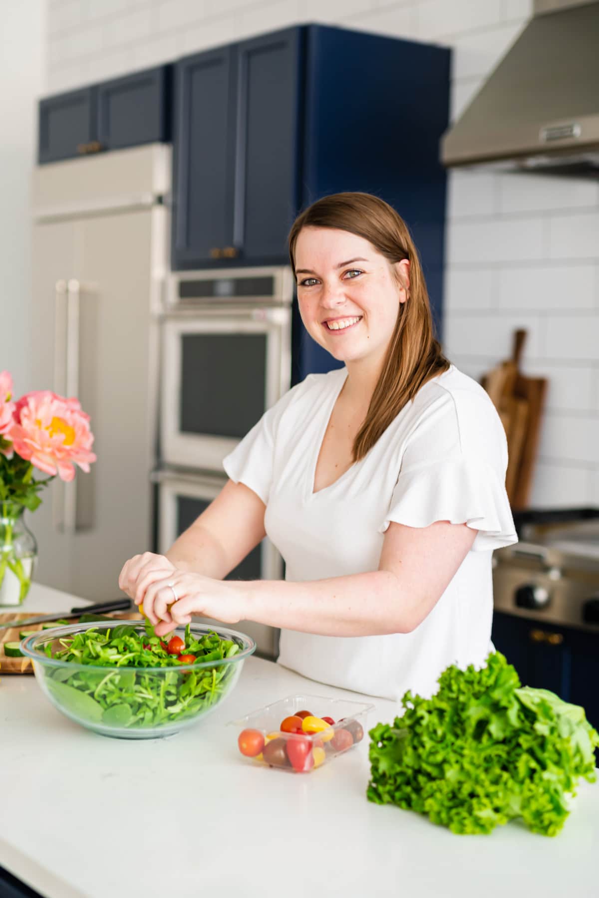 A woman in a white shirt placing tomatoes into a salad.