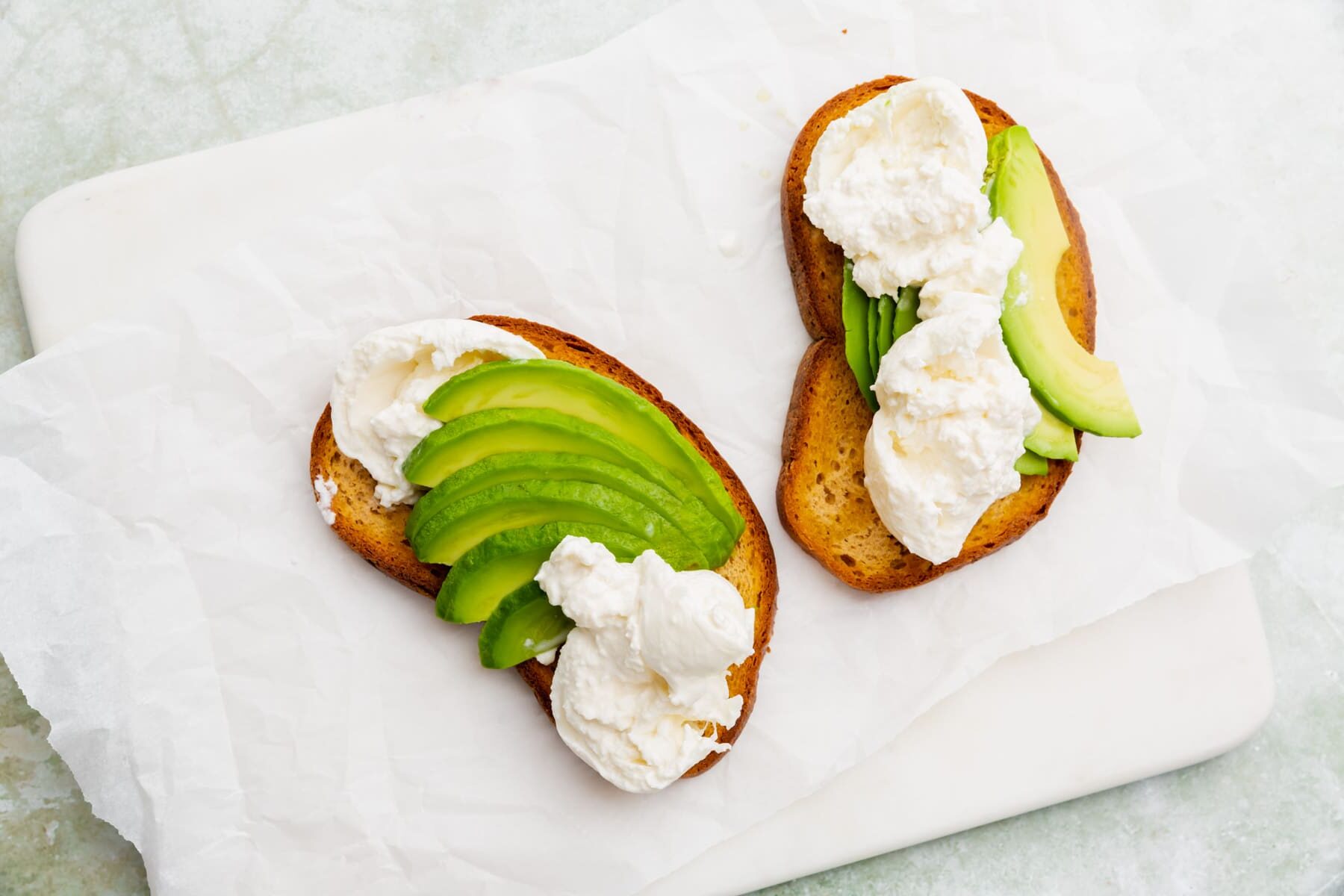 Two slices of avoacdo toast topped with burrata.