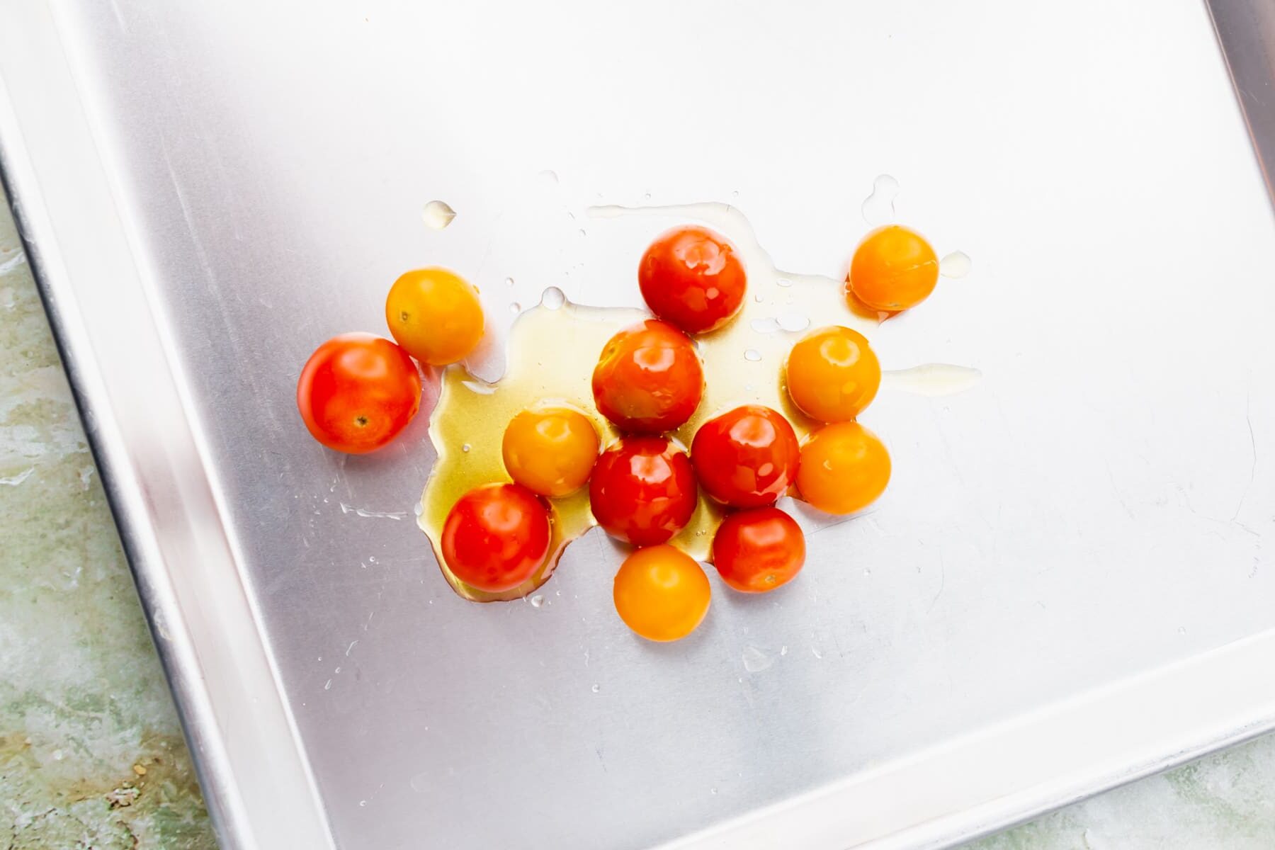 Colorful cherry tomatoes drizzled with olive oil on a sheet pan.