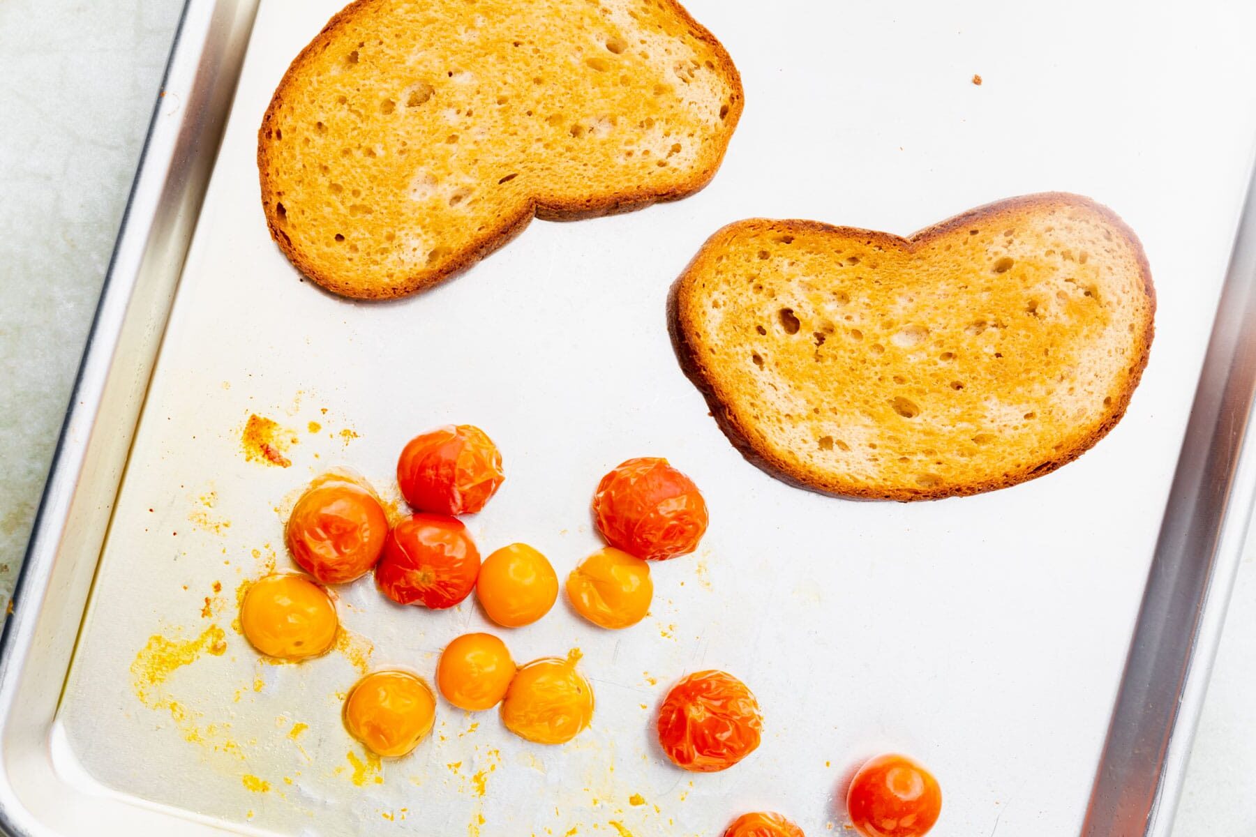 Roasted tomatos and sourdough bread on a sheet pan.