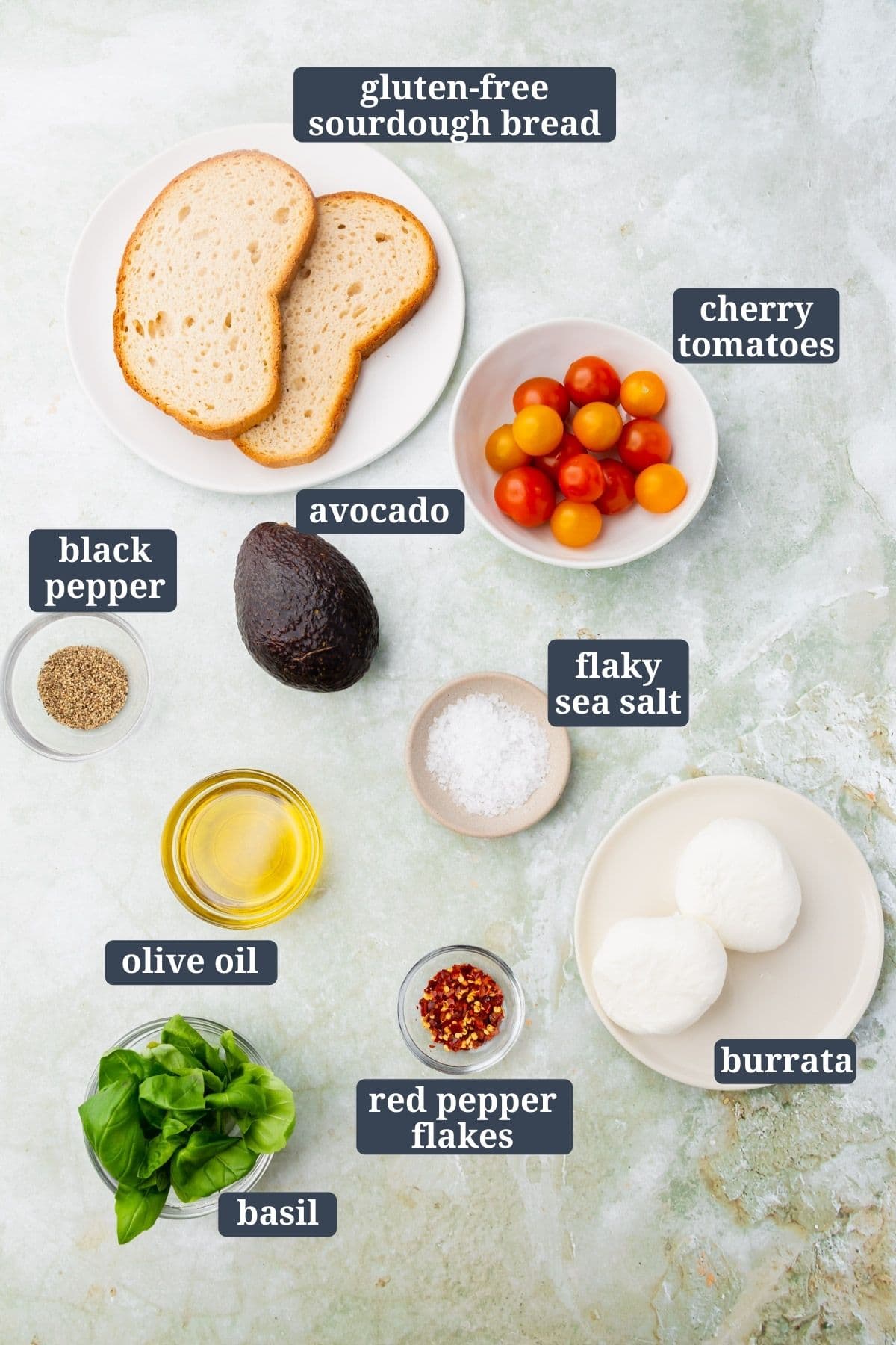 Ingredients for making gluten-free avocado burrata toast on a green marble table.