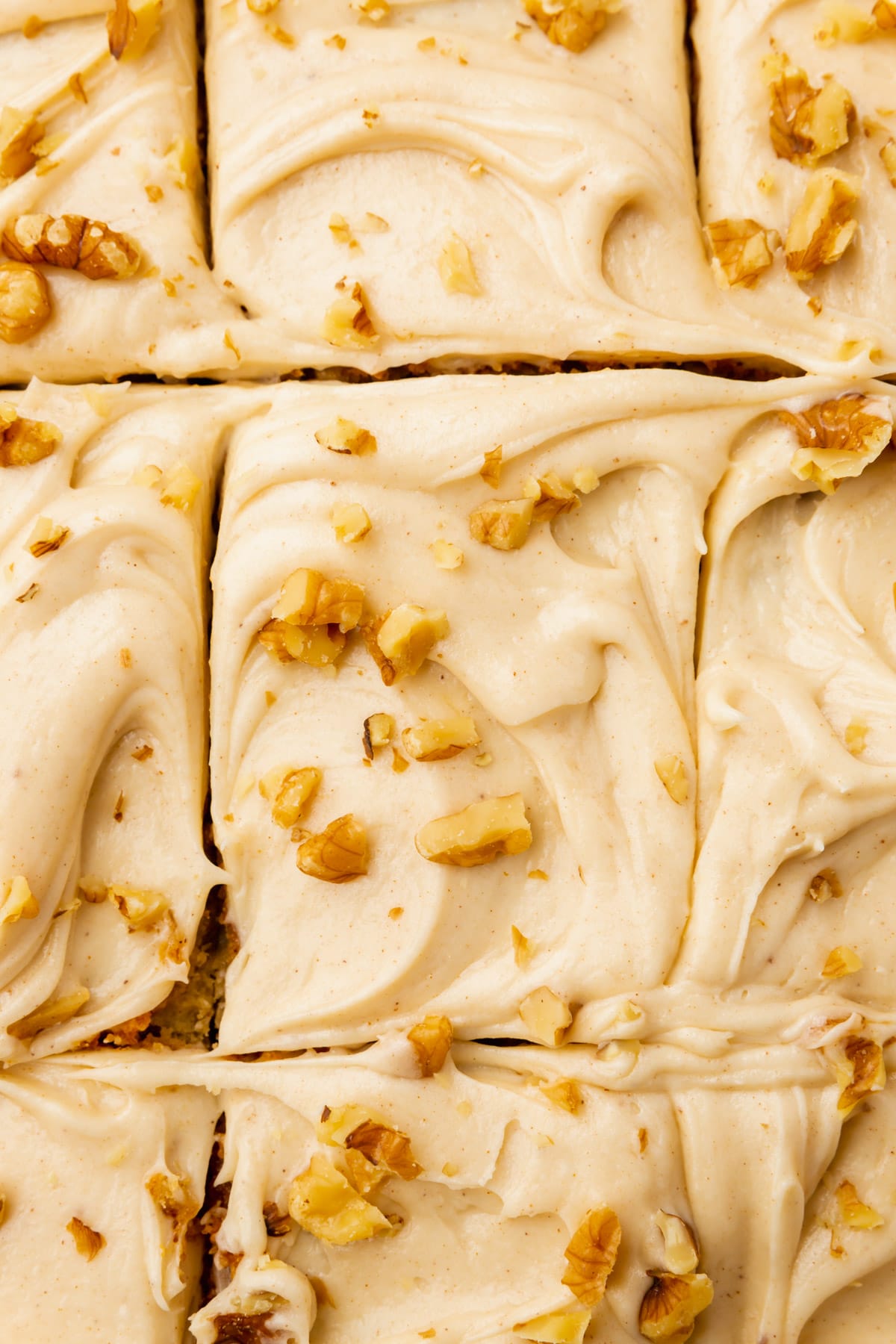 A closeup of cream cheese frosted cake slices topped with chopped walnuts.