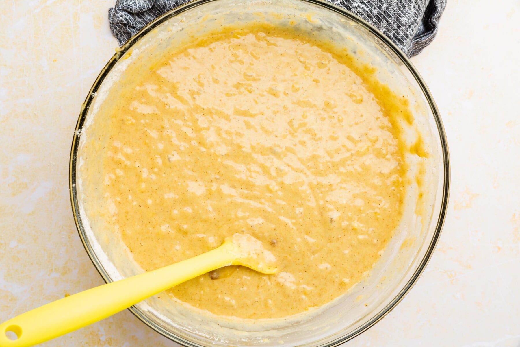 Gluten-free banana cake batter in a glass mixing bowl with a yellow spatula.