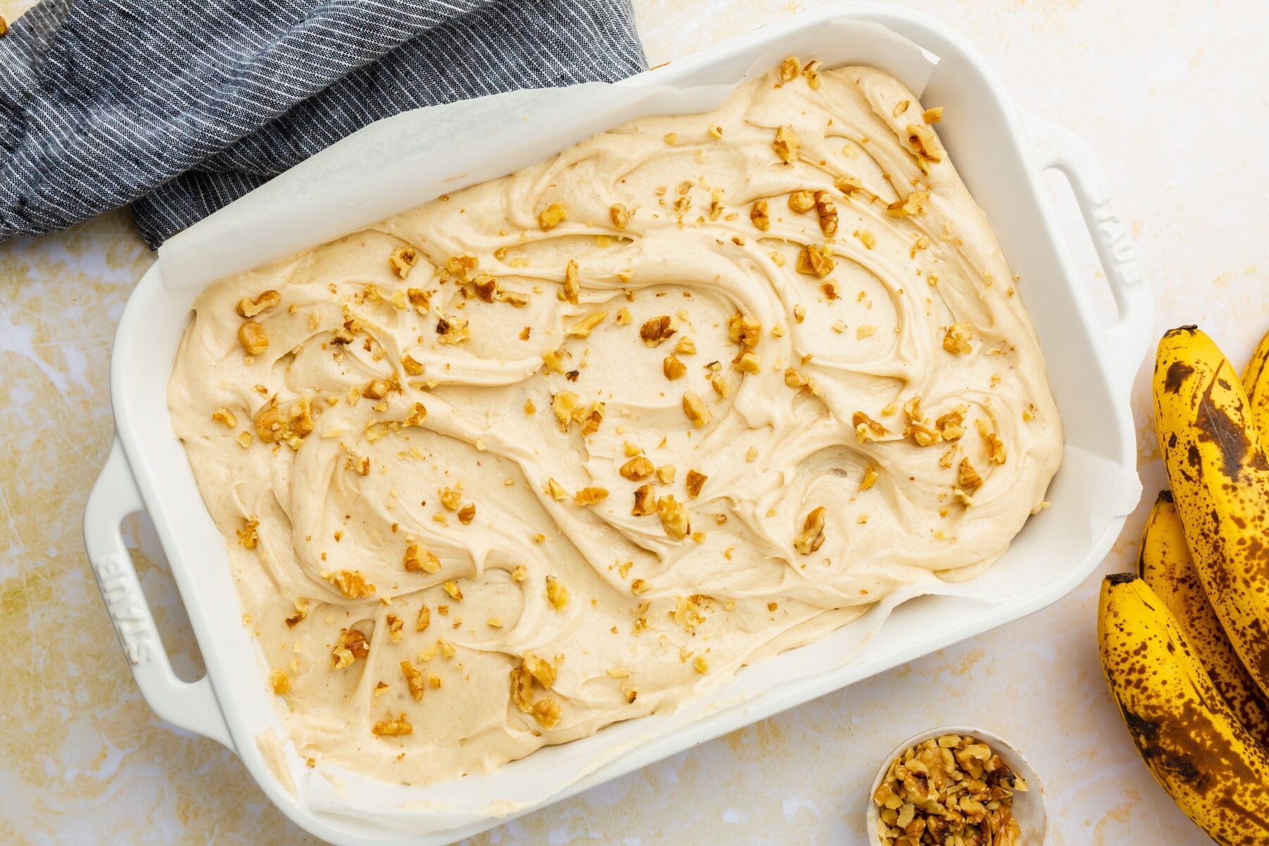 Gluten-free banana cake topped with cream cheese frosting and walnuts on a yellow table.
