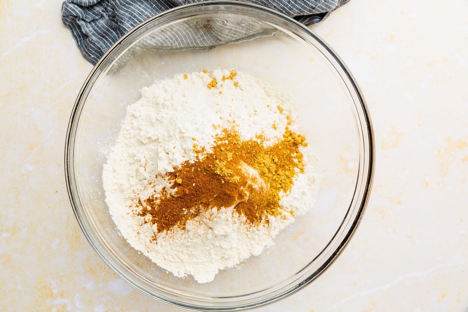 Gluten-free flour, cinnamon, ginger and nutmeg in a glass mixing bowl.