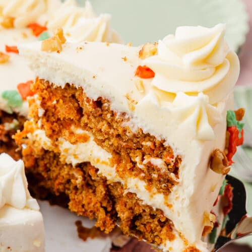 A slice of carrot cake being removed from a full cake with a green plate behind it.
