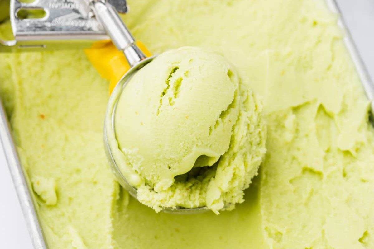 A yellow ice cream scooper scooping avocado ice cream from a loaf pan.