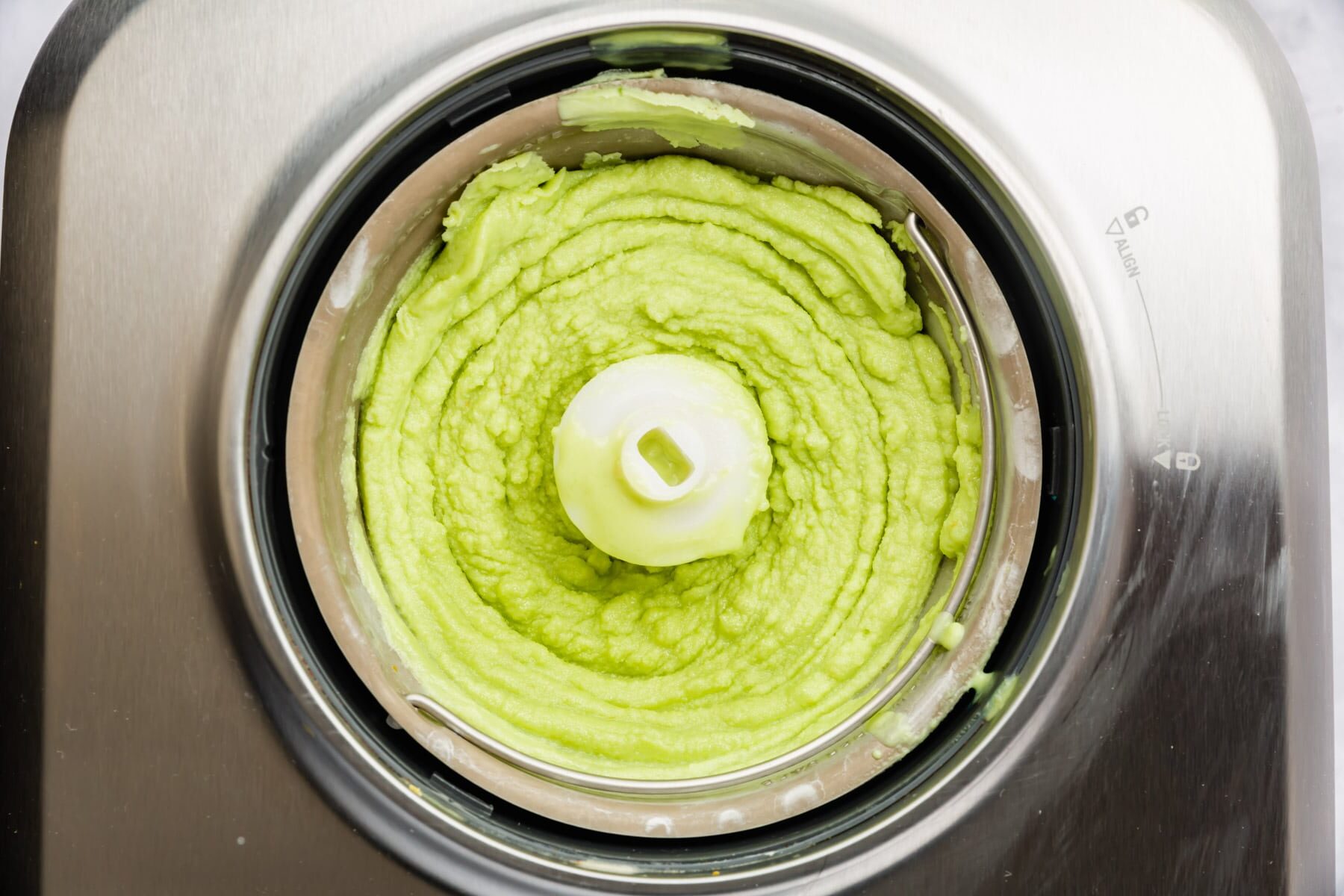 Churned avocado ice cream in the bowl of an ice cream maker.