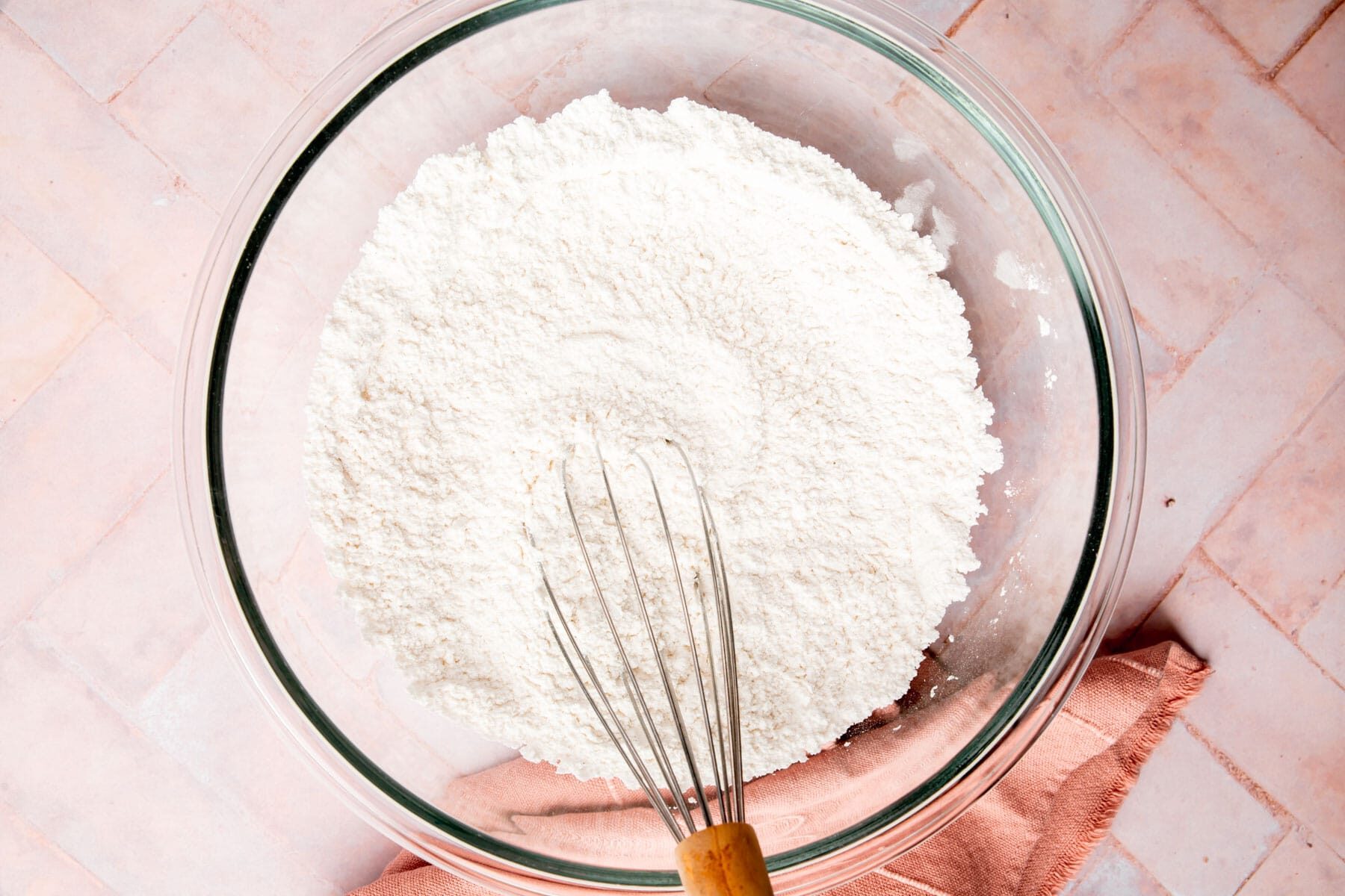 Gluten-free flour and powdered sugar in a glass mixing bowl with a whisk.