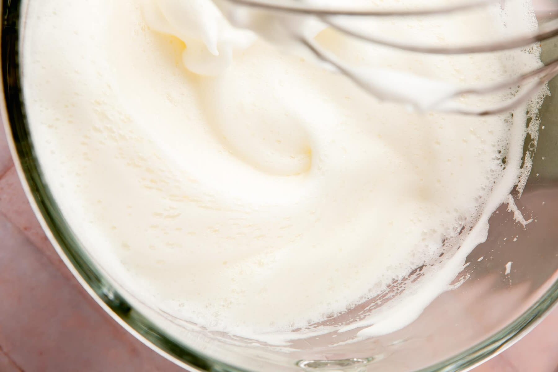 Egg whites and cream of tartar being whipped with a whisk attachment in a stand mixer.