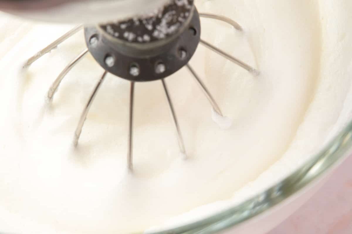A stand mixer with the whisk attachment whipping egg whites and sugar.