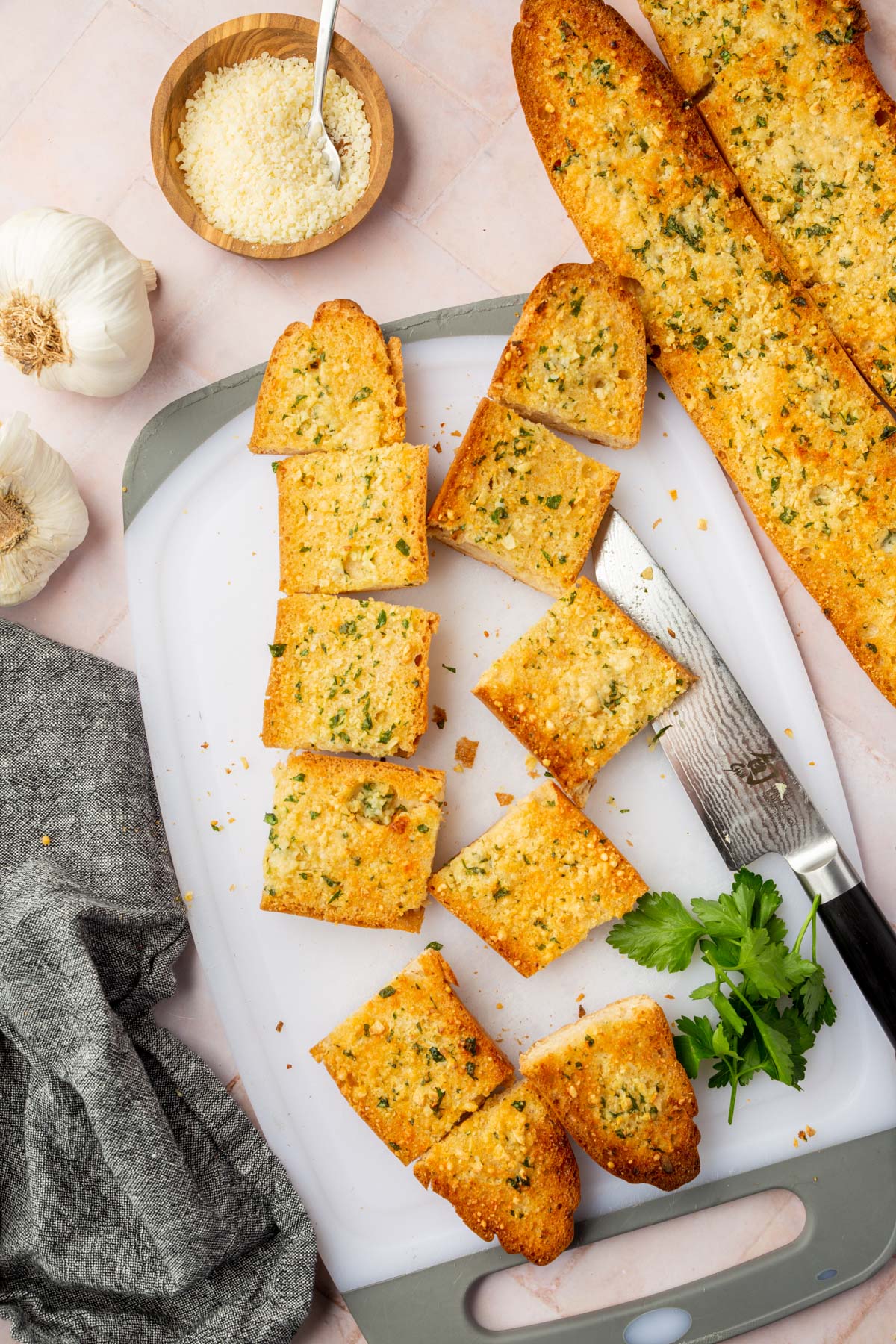 Baked golden garlic bread baguettes being sliced on a cutting board. 