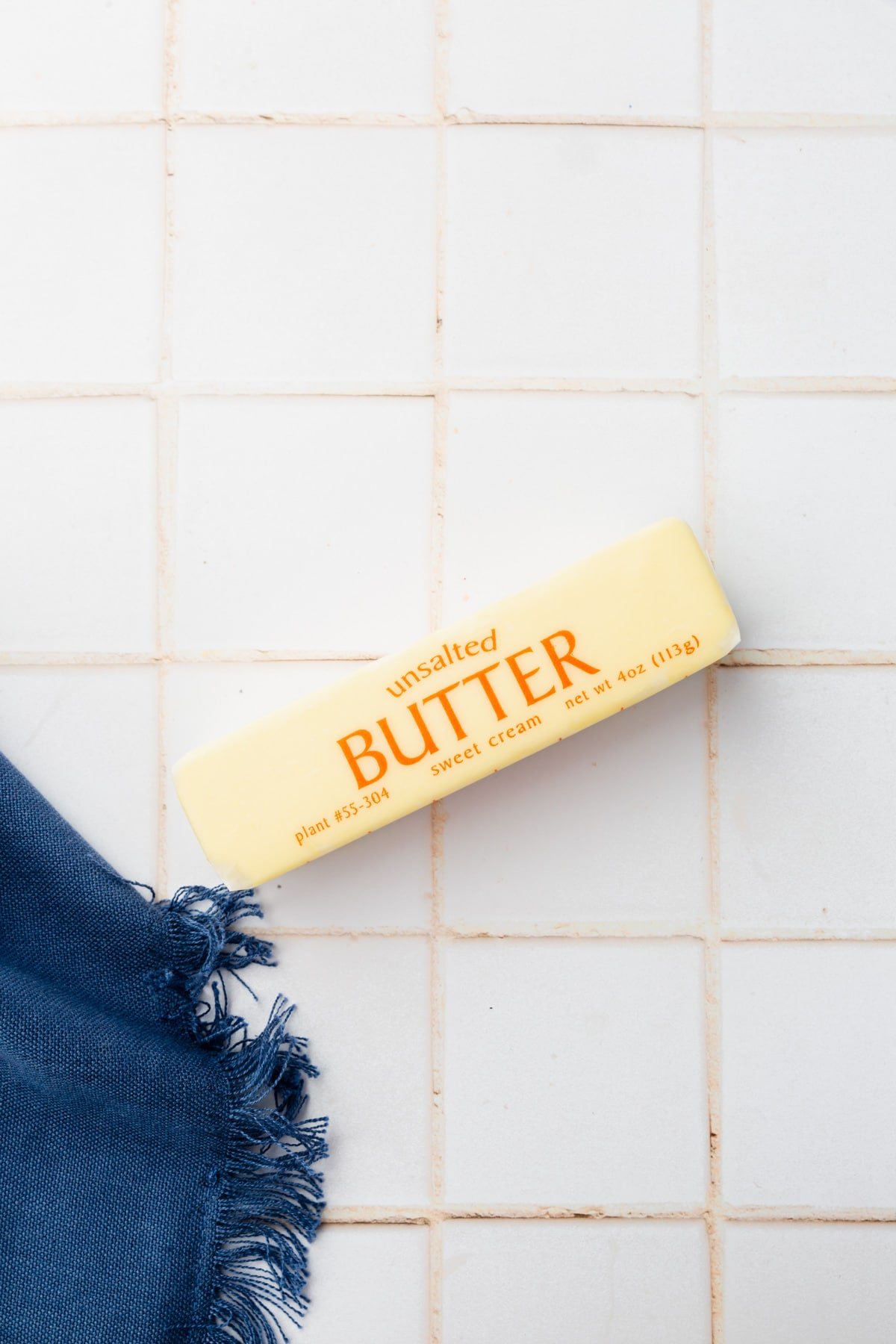 A stick of unsalted butter in the wrapper on a tile countertop. 