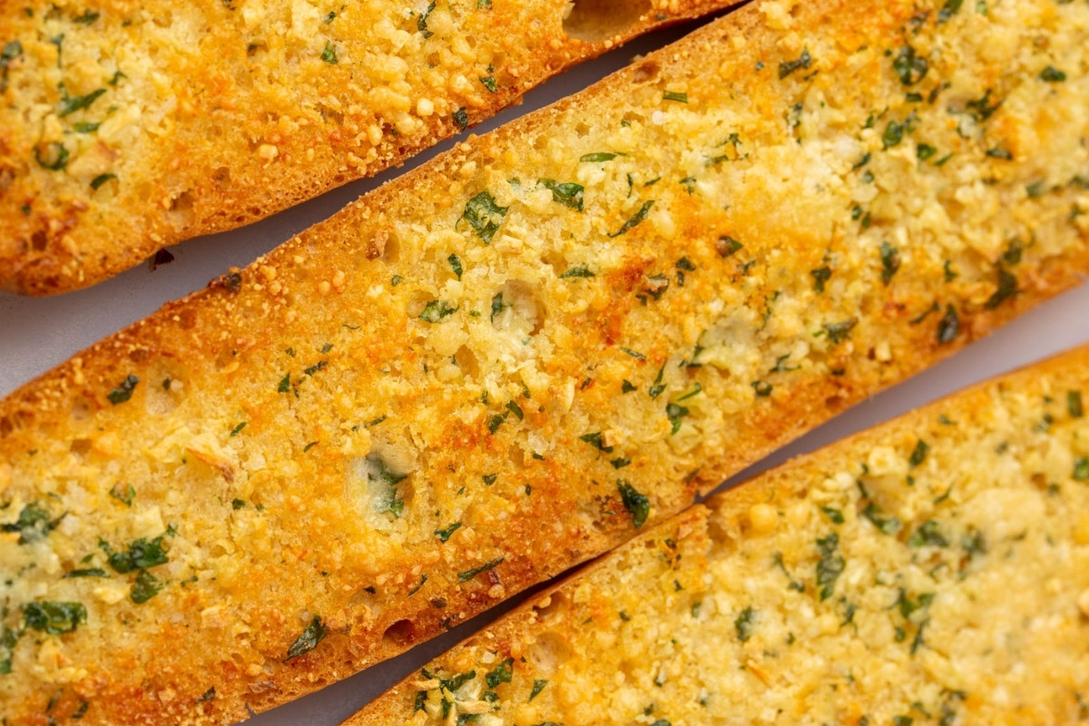 Close-up of several slices of golden, crispy Gluten Free Garlic Bread topped with chopped parsley and melted cheese, showing a crunchy texture and savory seasoning.