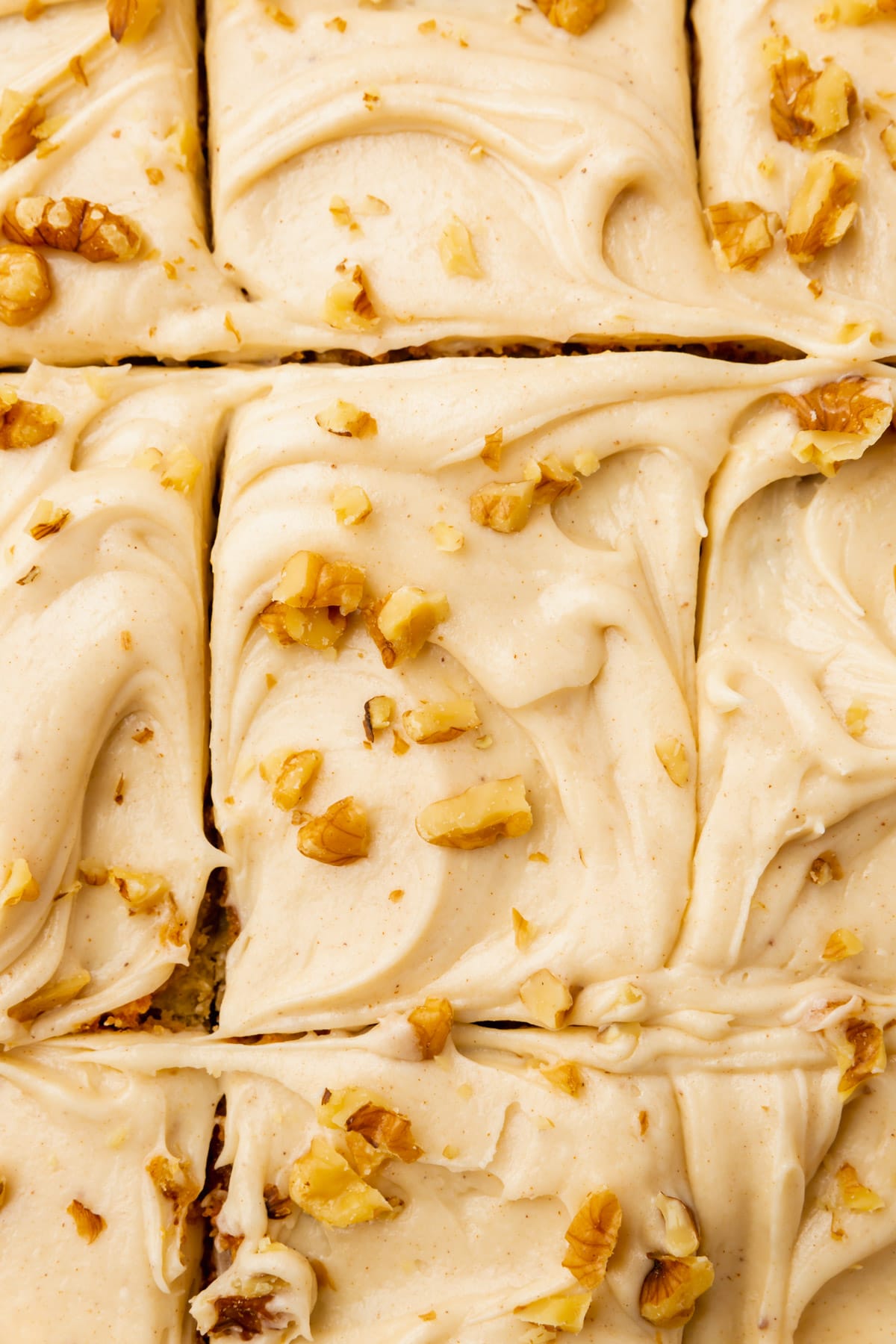 A sheet cake covered with brown butter cream cheese frosting and toasted walnuts that has been sliced into squares.