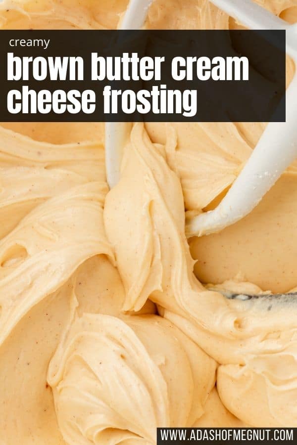 A glass mixing bowl with brown butter cream cheese frosting in it with a paddle attachment from the mixer in the bowl.