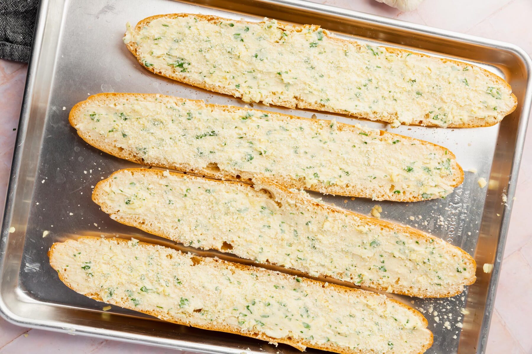 Gluten-free baguettes on a baking sheet slathered with garlic butter.
