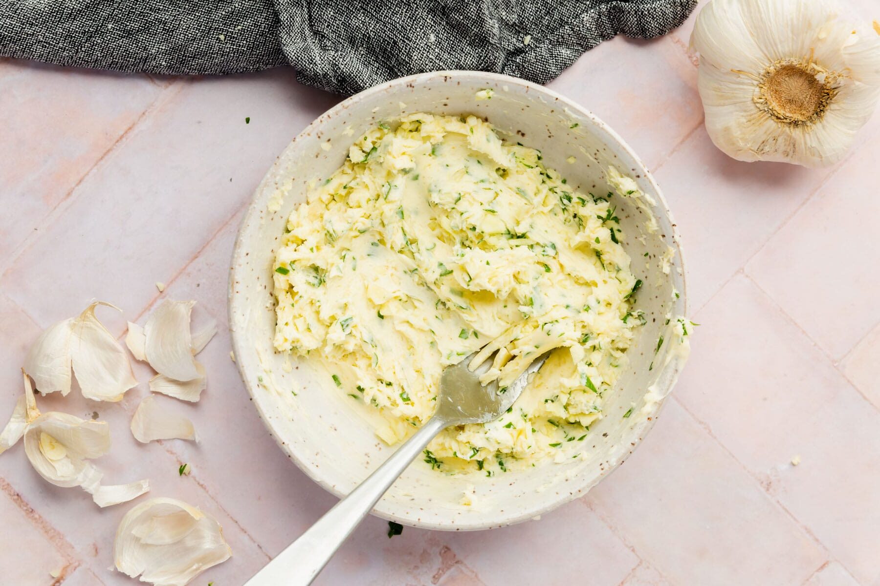 Garlic parsley butter in a bowl with a fork with a garlic bulb next to it.