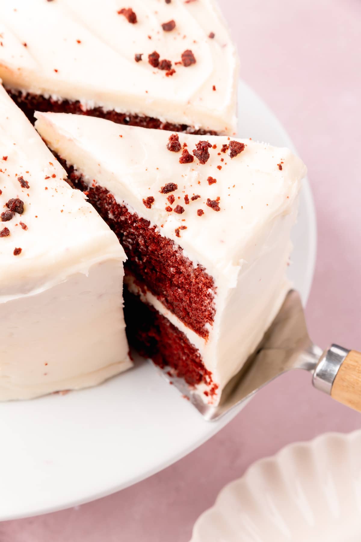 A slice of red velvet cake being pulled from the rest of the cake with a cake server.