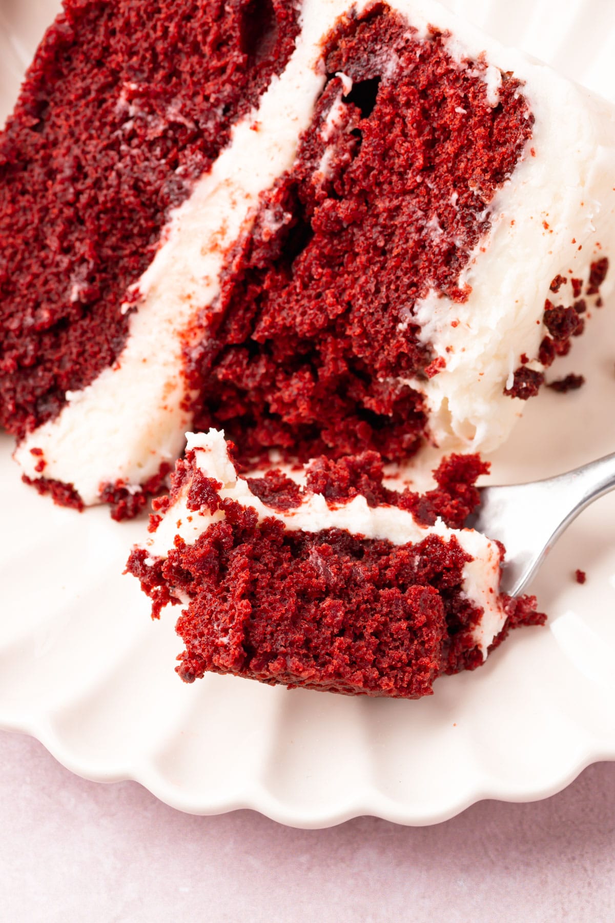 A piece of red velvet cake on a plate with a fork digging into the cake.