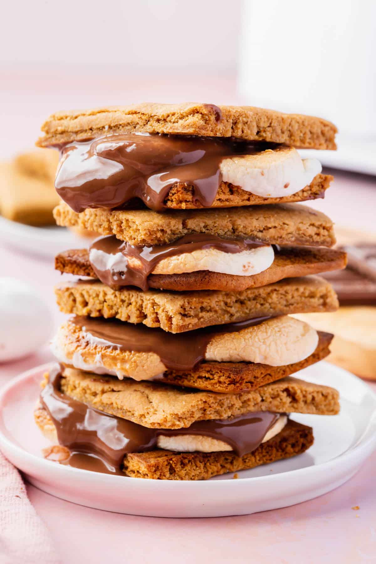 A stack of four air fryer s'mores on a small plate with an air fryer in the backgorund.
