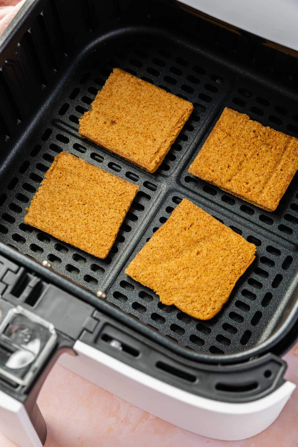 An air fryer basket with four gluten-free graham cracker squares in it.