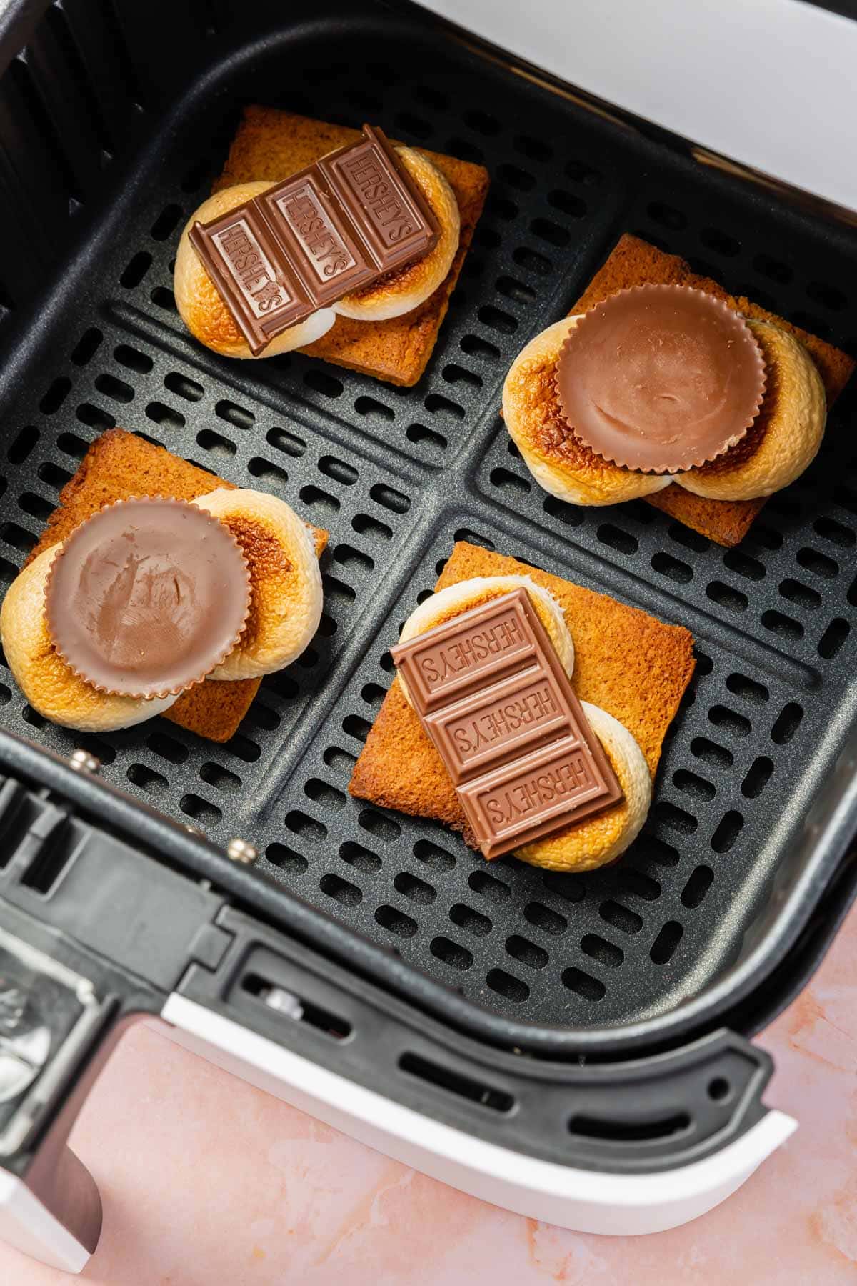 An air fryer basket with four open-face s'mores in it.