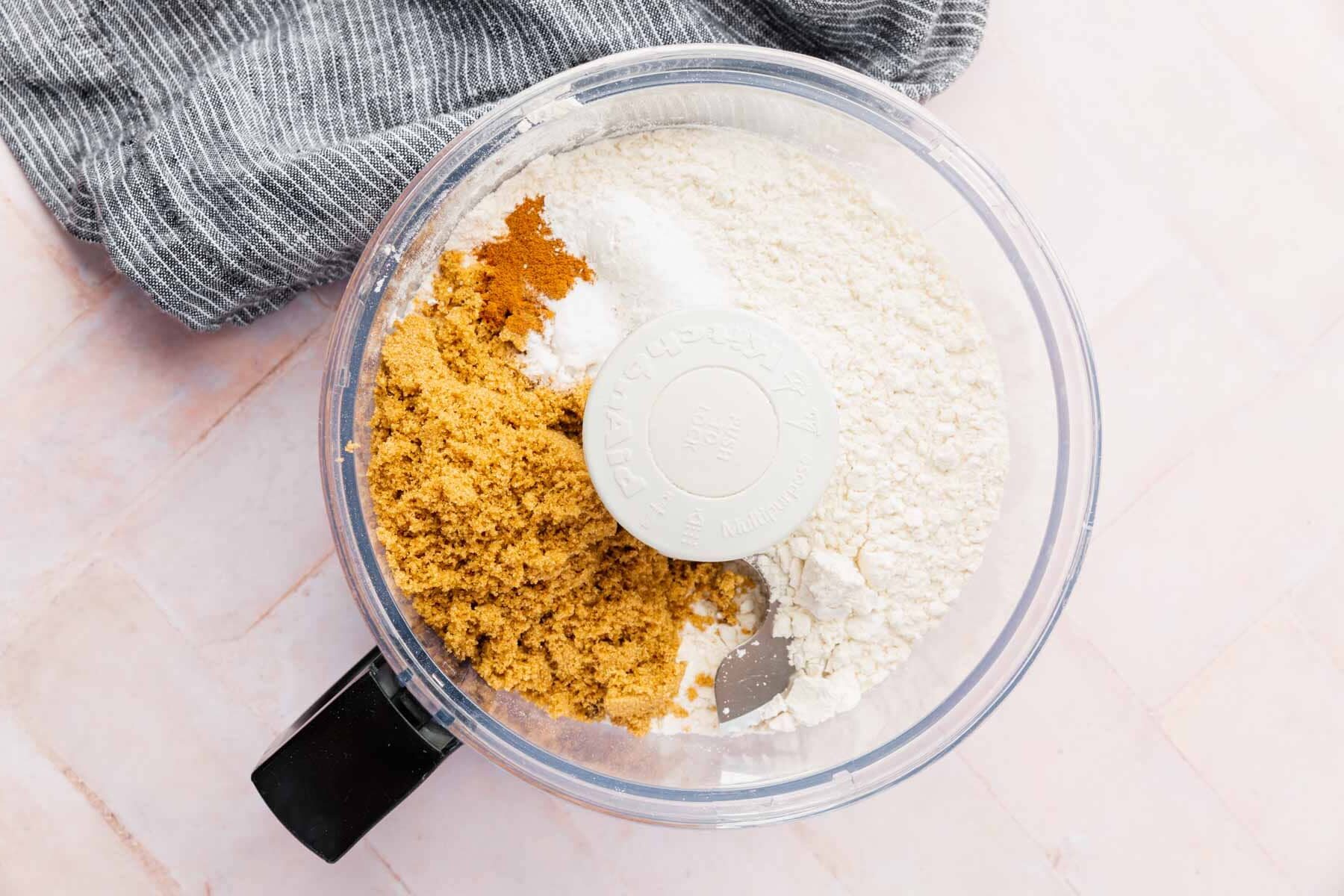 A food processor with gluten-free flour, brown sugar, salt, and cinnamon in it.