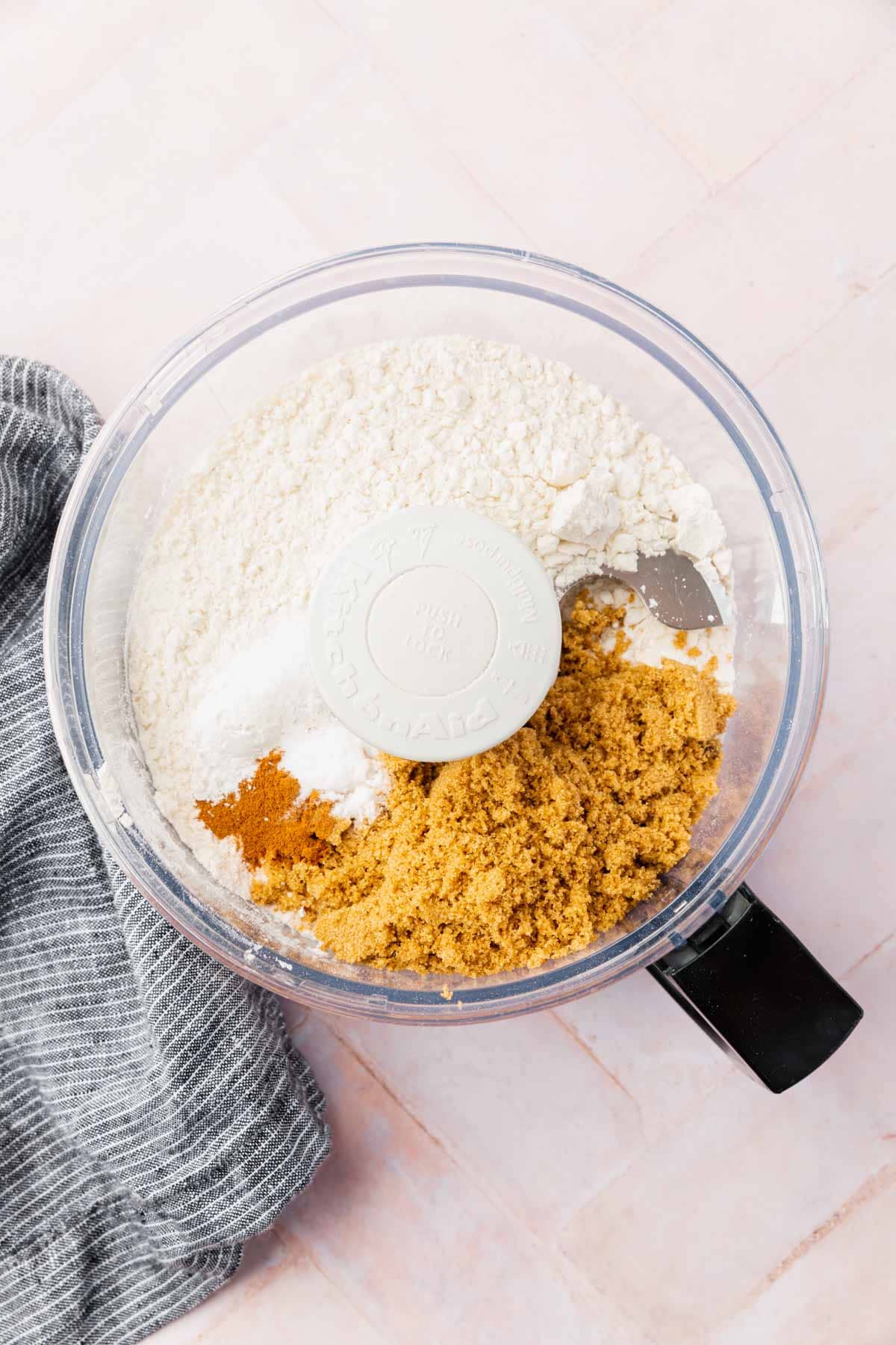 A food processor with gluten-free flour, brown sugar, salt, and cinnamon in it.