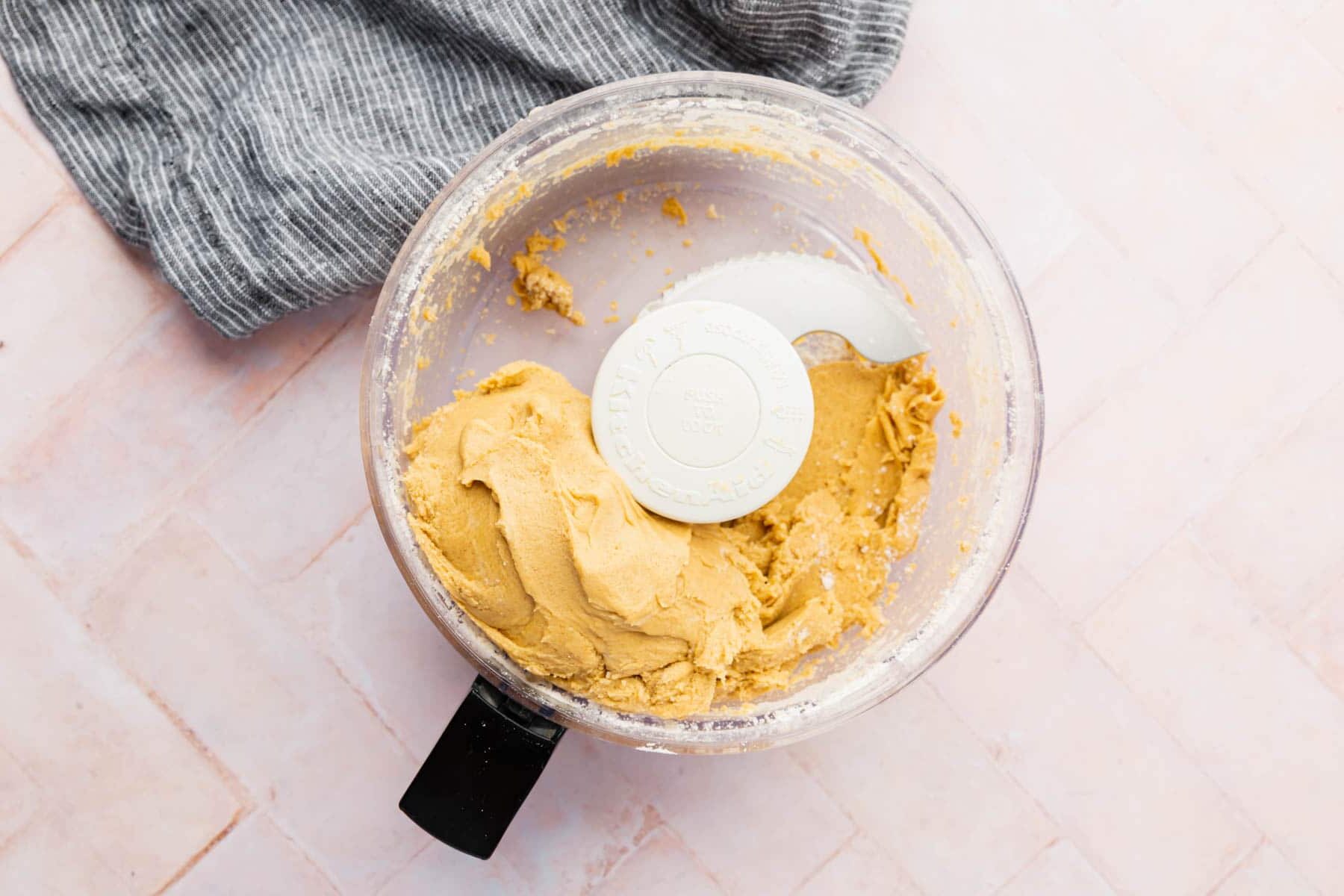 A food processor with a blade in it with gluten-free graham cracker dough.