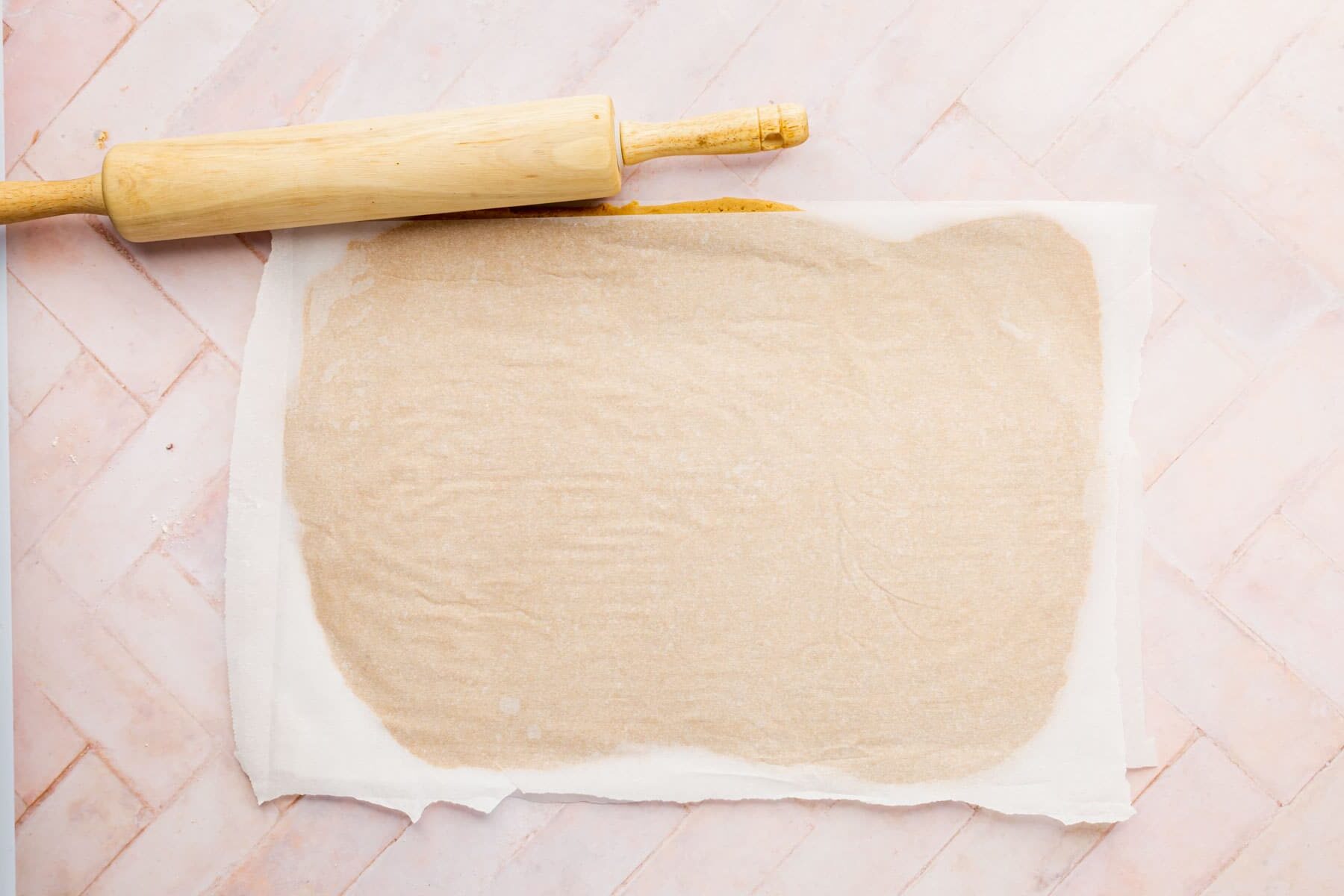 Graham cracker rolled out with a piece of parchment paper on top of it with a rolling pin next to it.
