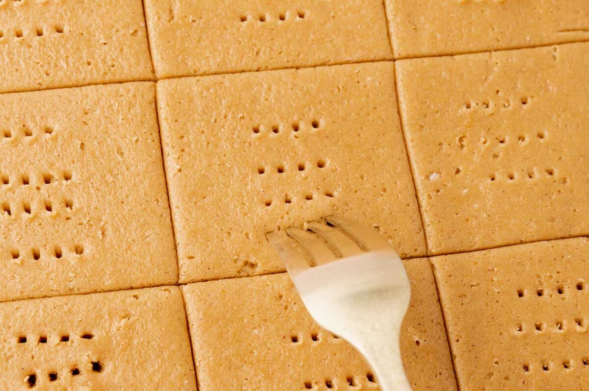 A fork poking holes into graham cracker dough.