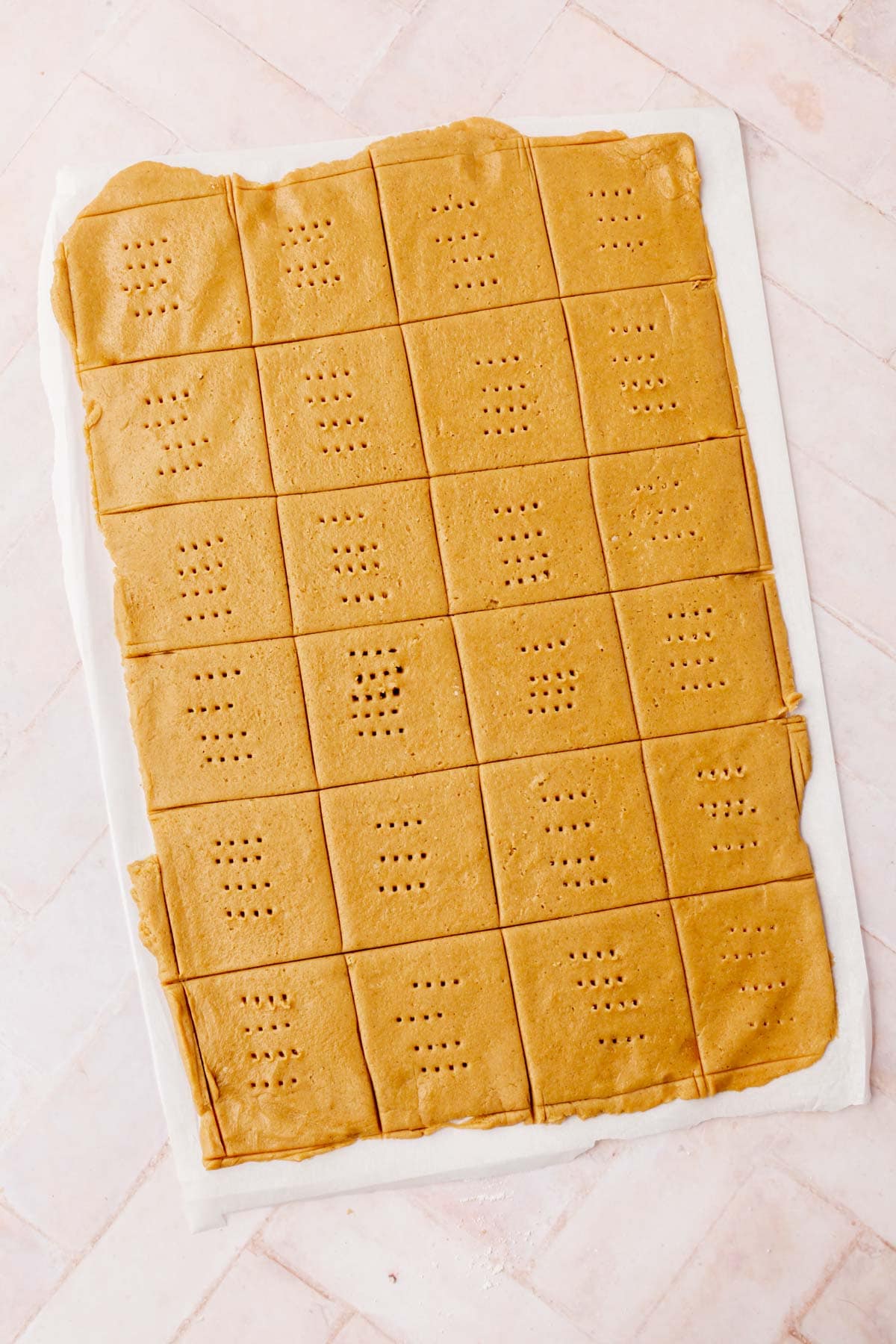 Graham cracker dough cut into squares with fork holes on a piece of parchment paper.
